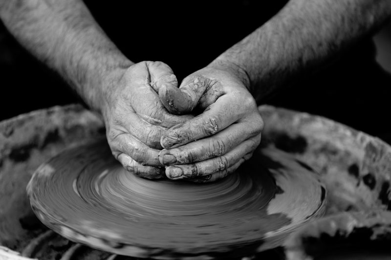 A pair of hands shaping clay using a pottery wheel
